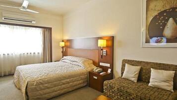 Una habitación de hotel con cama, sofá, mesita de noche y lámpara de pared.