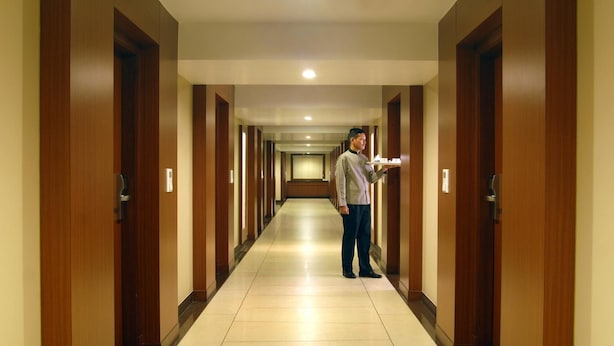 Un pasillo de hotel con puertas de madera, piso de baldosas y una persona de pie en el centro.