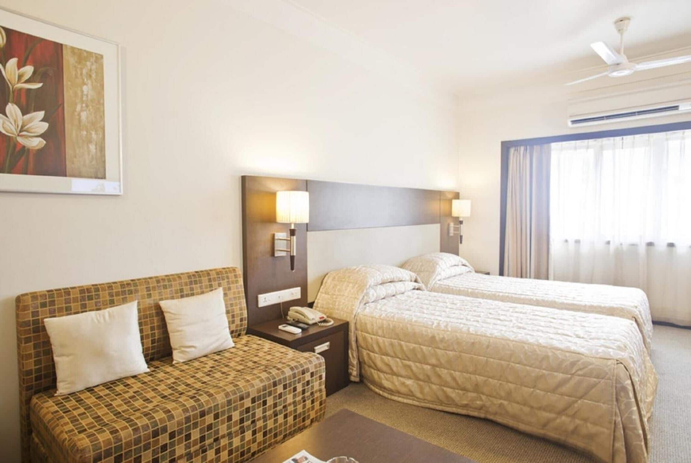 A hotel room with two beds, a sofa, a nightstand with a phone, and a painting on the wall.