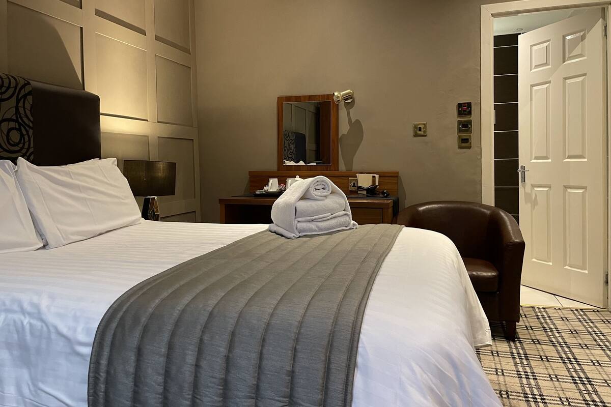 Een hotelkamer met een groot bed, een bureau met spiegel, een stoel en een kledingkast.