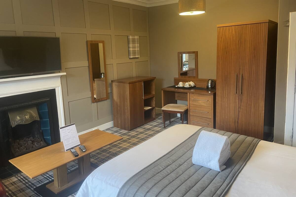Een hotelkamer met een bed, bureau, spiegel, kledingkast en open haard.