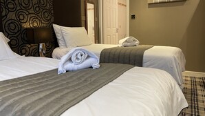 Une chambre d’hôtel avec deux lits, une tête de lit à motifs, une table de chevet avec une lampe, une porte et un luminaire fixé au mur.