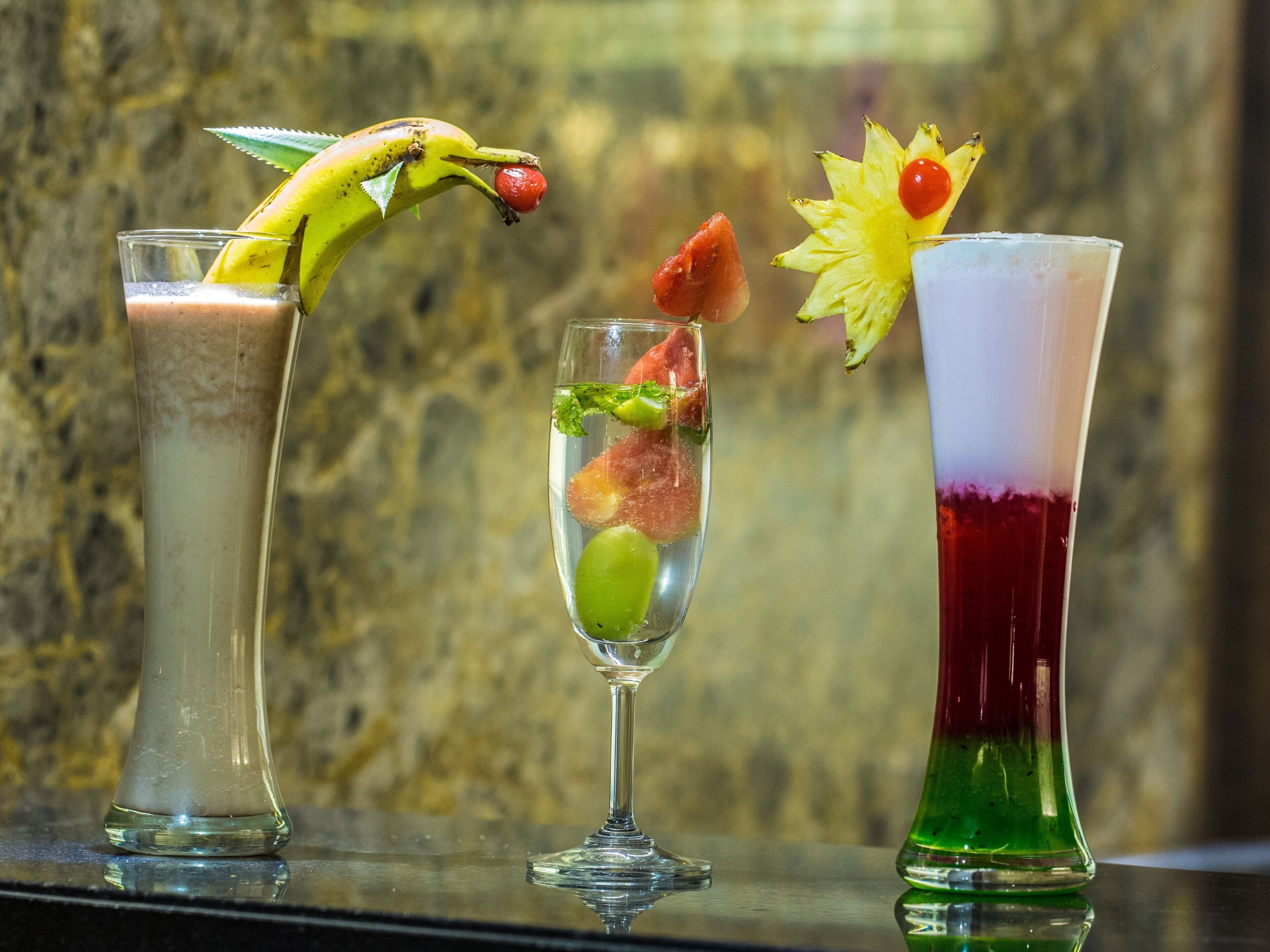 Three cocktails with various garnishes on a reflective surface.