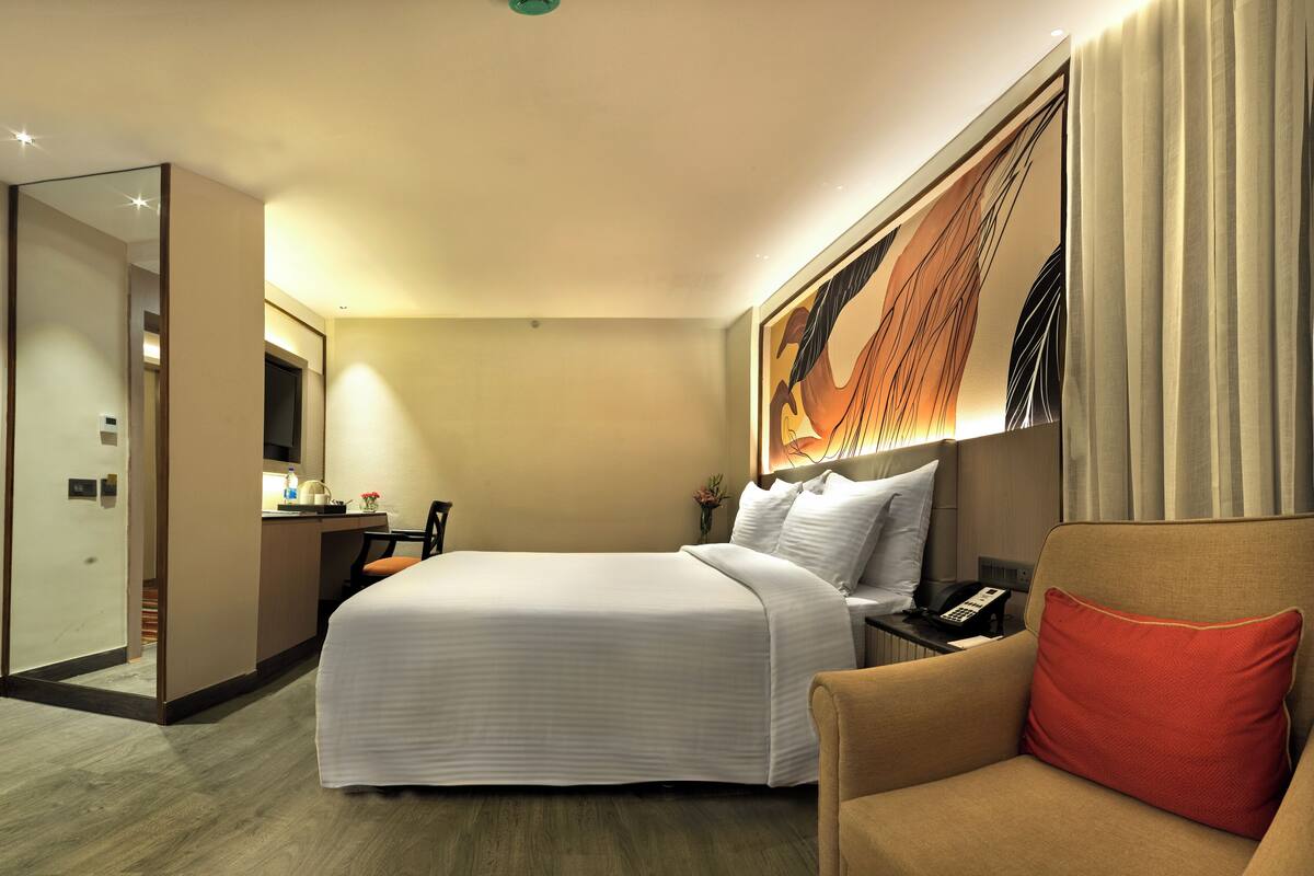 A hotel room with a bed, a desk with a chair, a telephone, and a mirror.