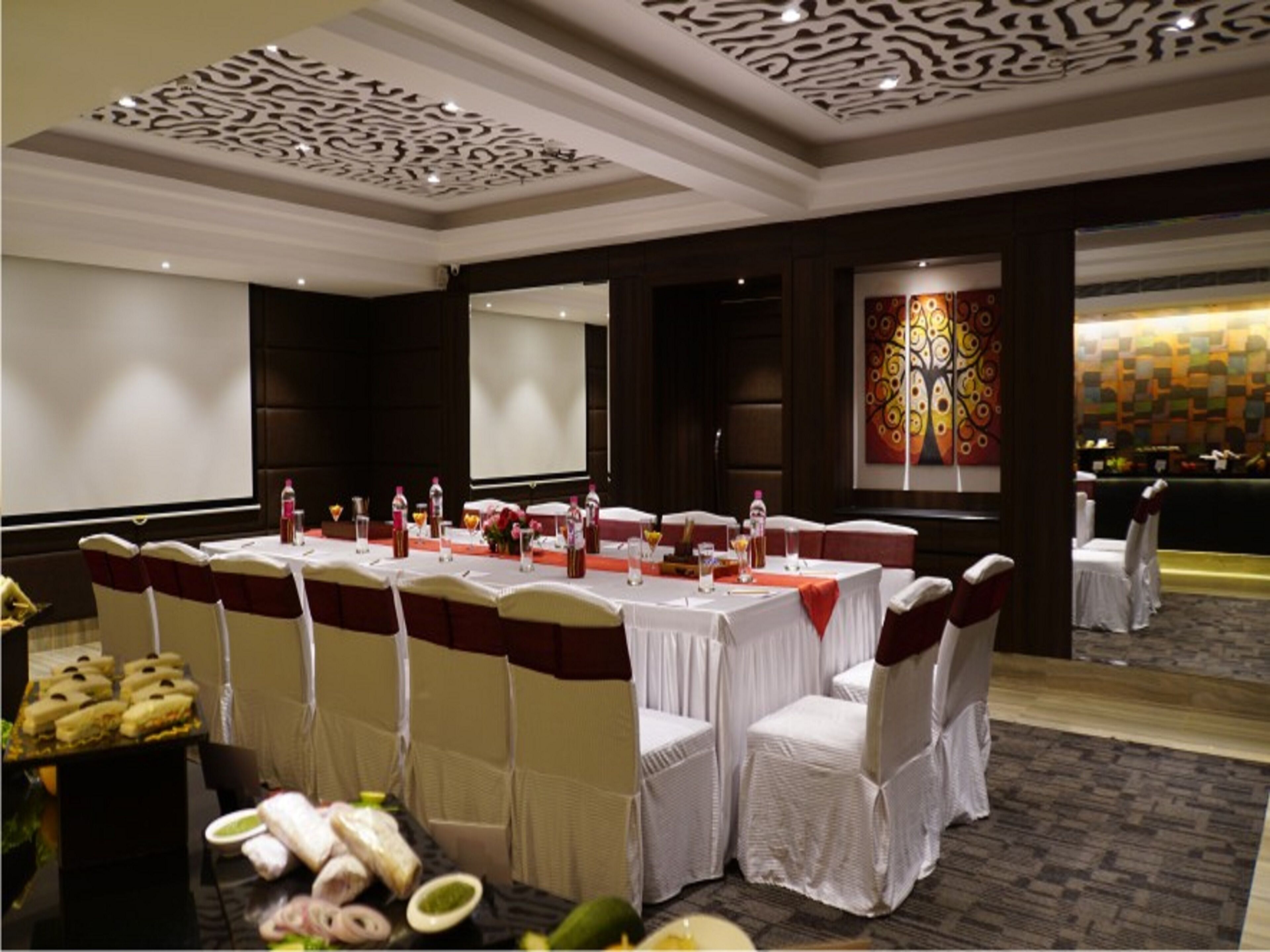 A conference room with a long table, white chairs, and a projector screen.