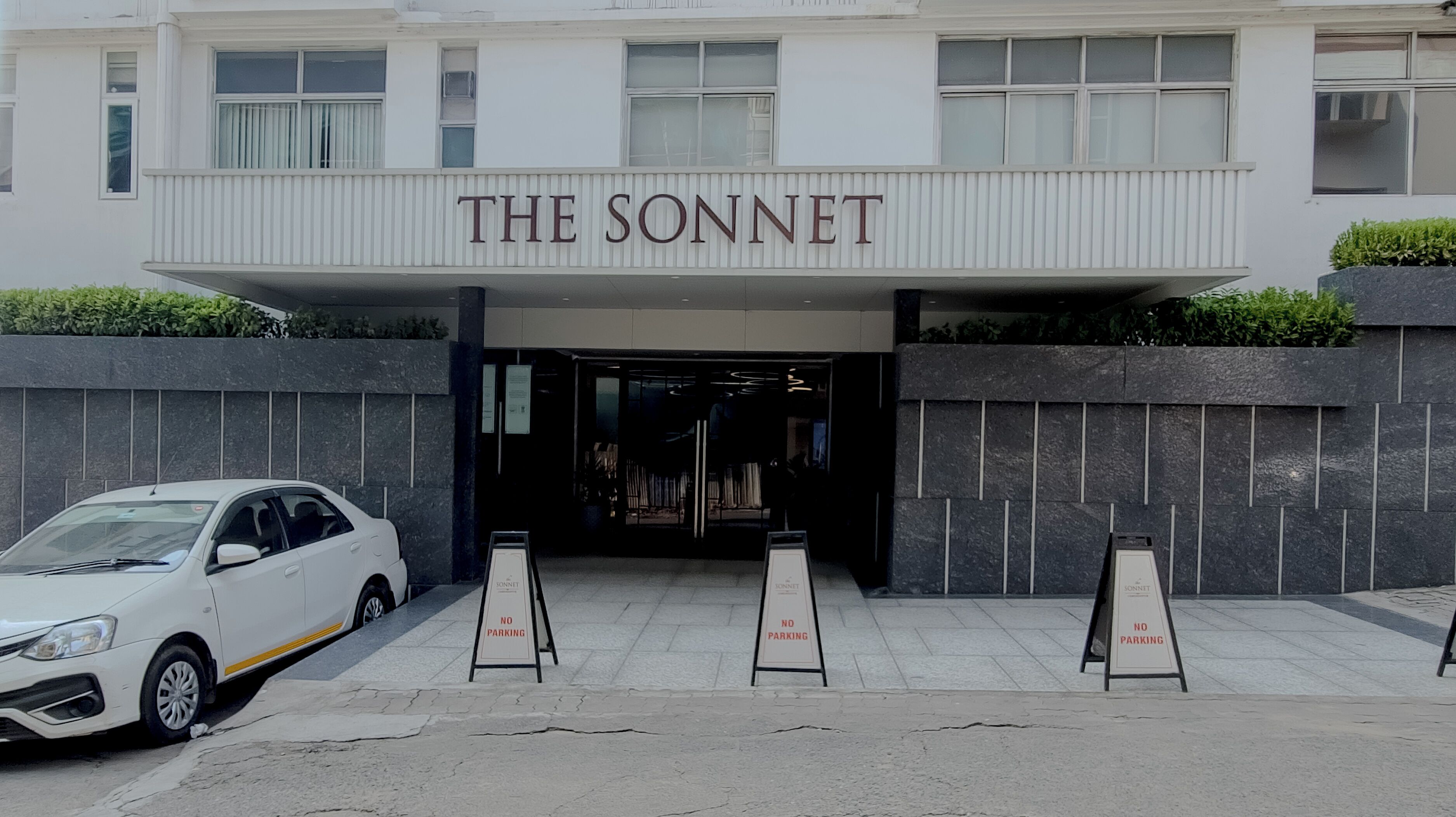 A building with a sign reading "THE SONNET" above the entrance. There are three "NO PARKING" signs in front.