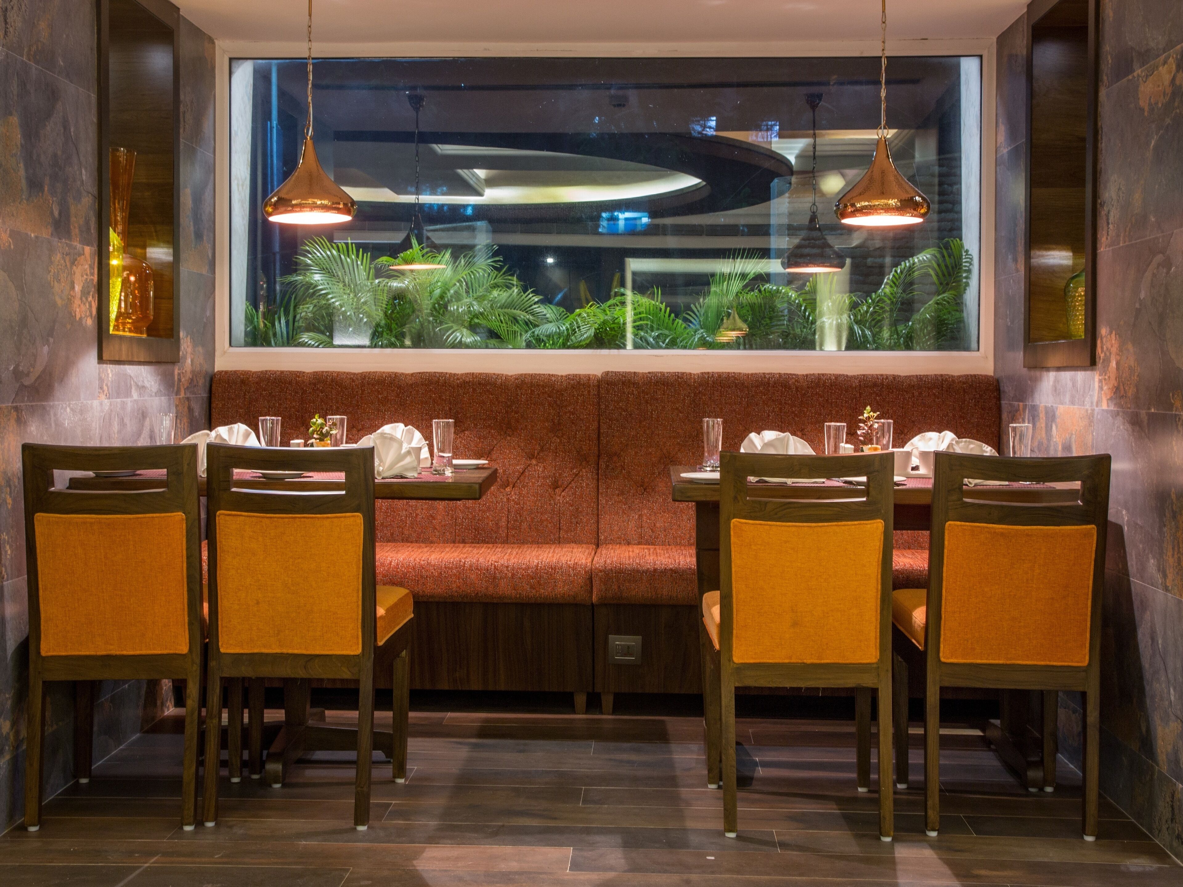 A restaurant with a booth seating area, wooden chairs with orange cushions, and pendant lighting.