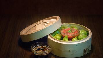 A bamboo steamer with green vegetables and a bowl of sauce.