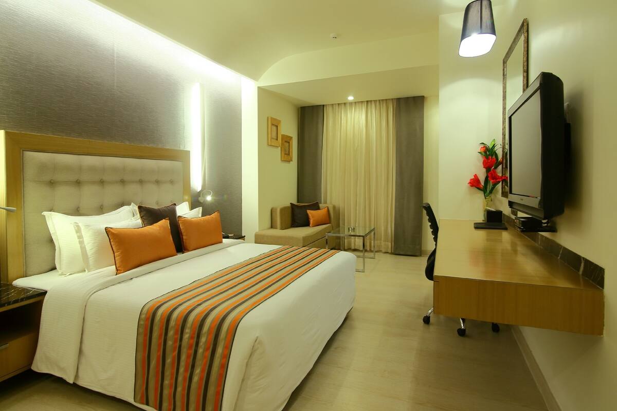 A hotel room with a large bed, a desk, a television, and a mirror.