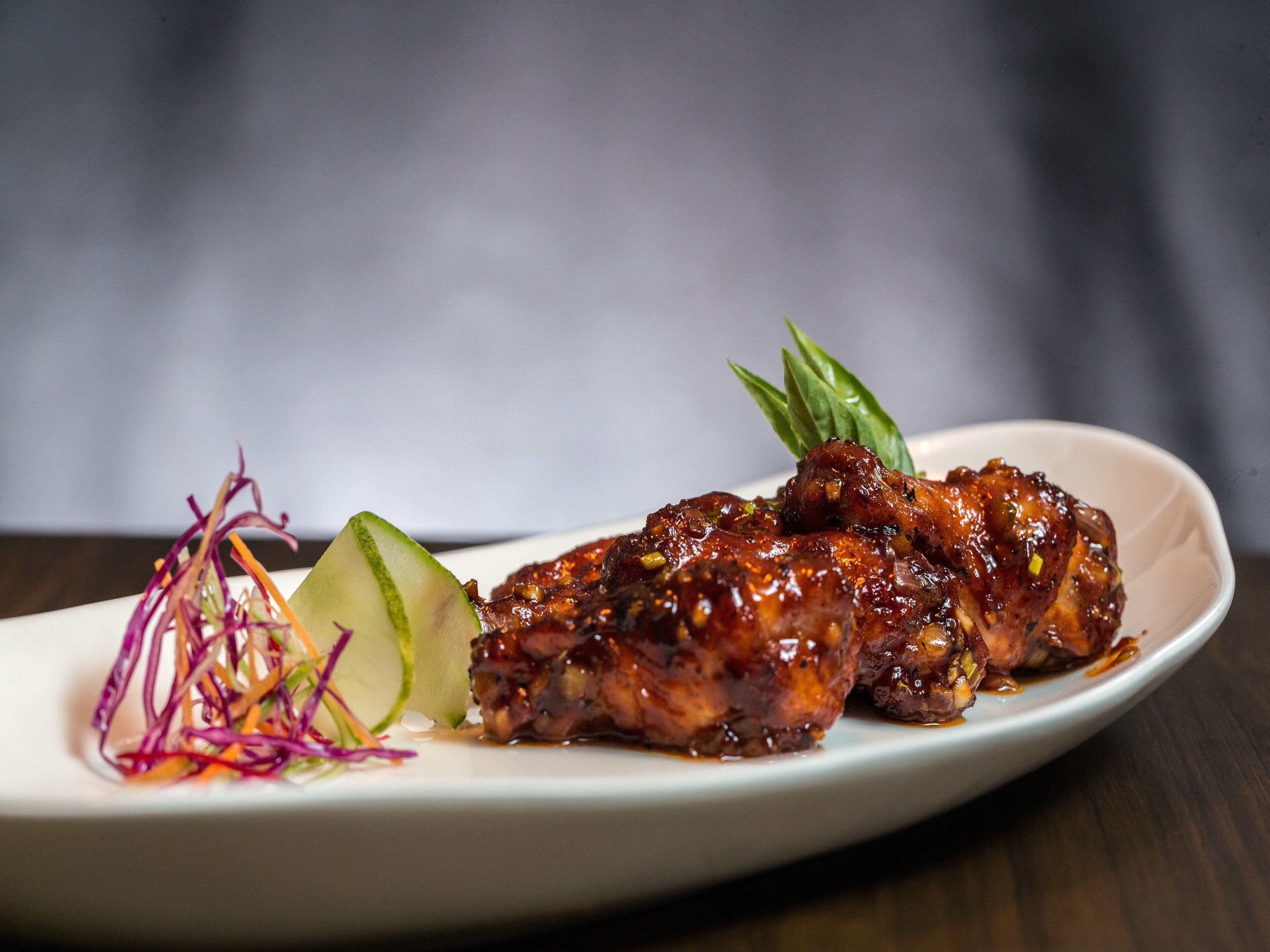 A plate with glazed chicken wings, a cucumber slice, and a colorful vegetable garnish.