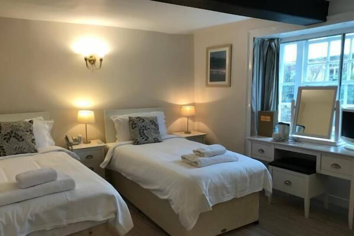 Ein Hotelzimmer mit zwei Betten, Nachttischlampen, einem Schreibtisch mit Spiegel und einem Fenster mit Vorhängen.
