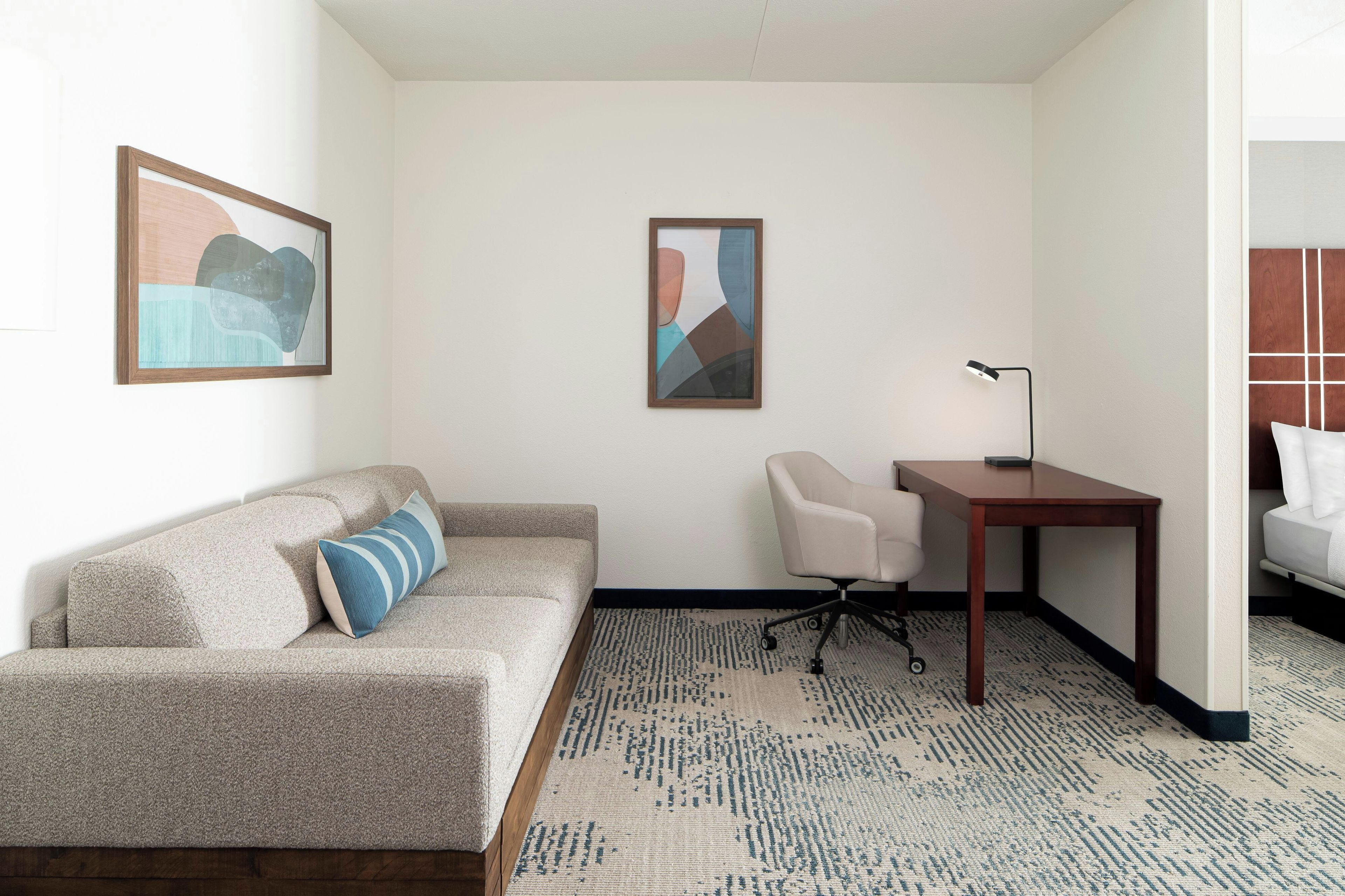 Ein Hotelzimmer mit einer Couch, einem Schreibtisch, einem Sessel und zwei abstrakten Bildern an der Wand.