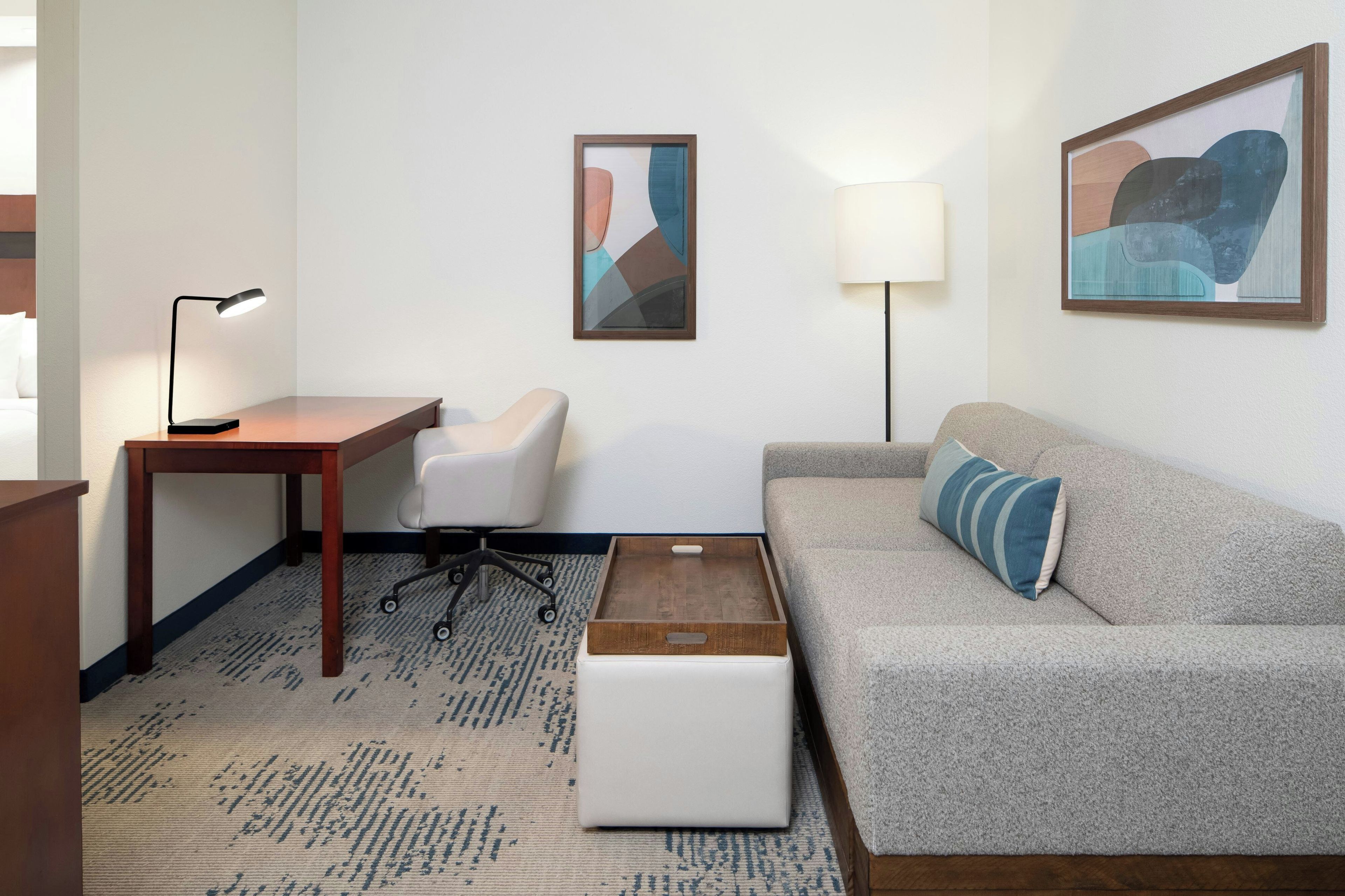 A hotel room with a desk, chair, sofa, and artwork on the walls.