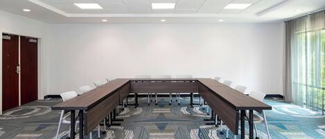 A conference room with a long table, white chairs, and a patterned carpet.