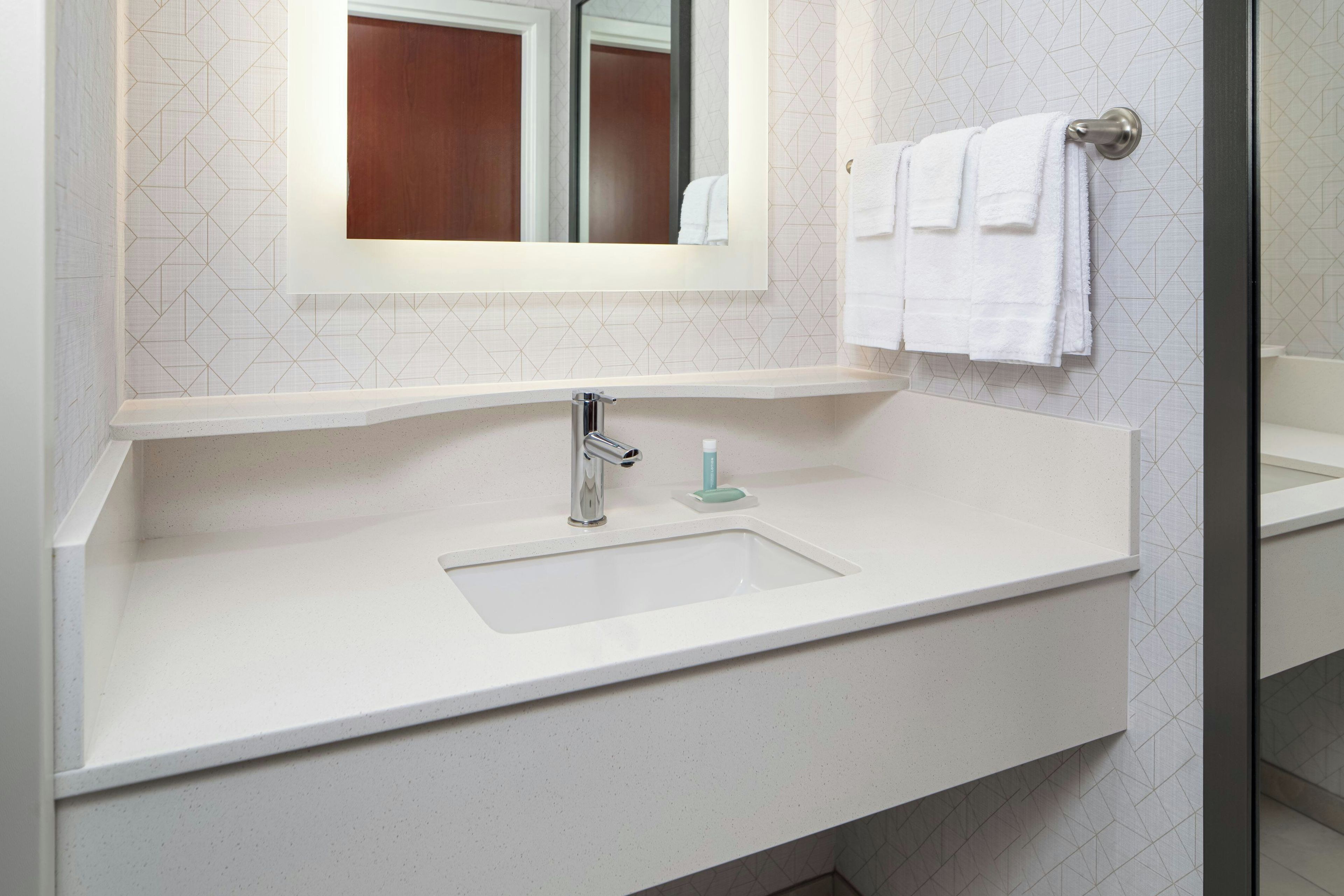 Un baño con lavamanos blanco, espejo y perchero.