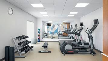 Un gimnasio con cintas de correr, elípticas, una banca, mancuernas y un espejo grande.