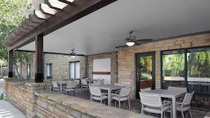 An outdoor patio with stone walls, multiple tables and chairs, and a ceiling fan.
