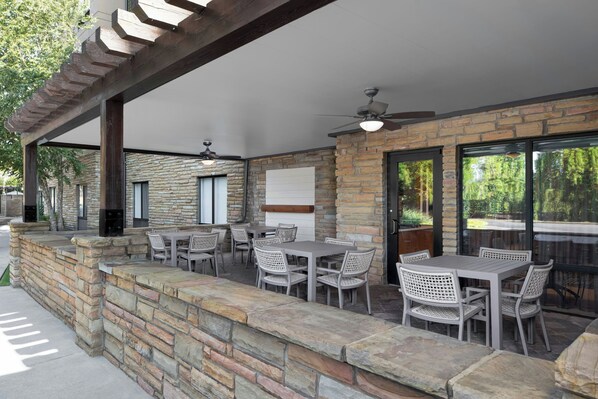 Une terrasse extérieure avec des murs en pierre, plusieurs tables et chaises, et un ventilateur de plafond.