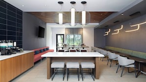 A modern dining area with a long table, multiple chairs, and a bar counter with coffee machines.