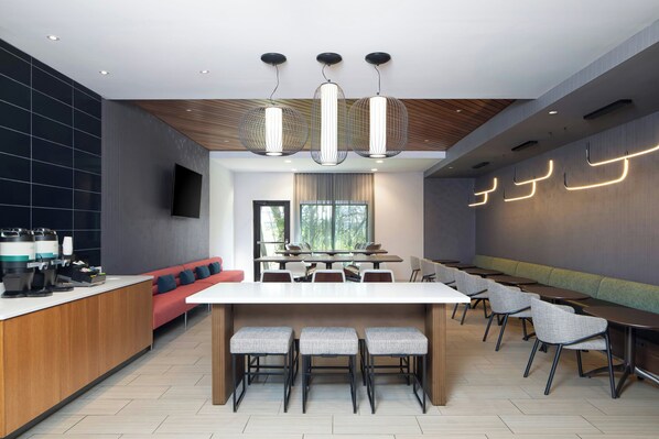 A modern dining area with a long table, multiple chairs, and a bar counter with coffee machines. - SpringHill Suites by Marriott Pigeon Forge (Pigeon Forge)
