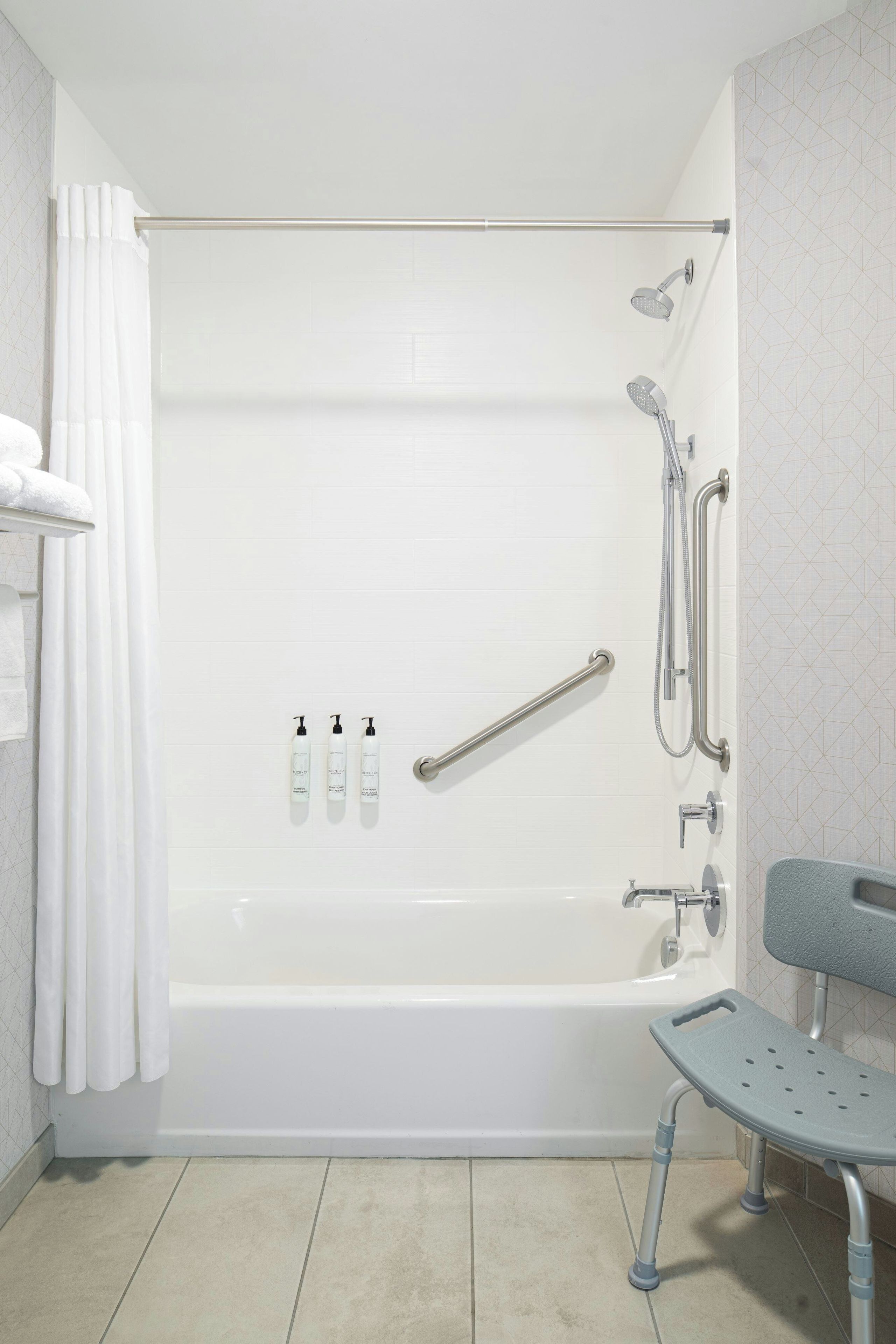 Un baño moderno con bañera, ducha y barras de apoyo. Hay tres botellas de champú en la pared.