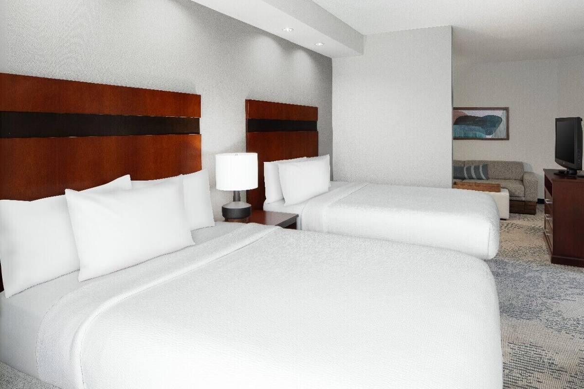 A hotel room with two beds, a TV, a sofa, and a painting on the wall.