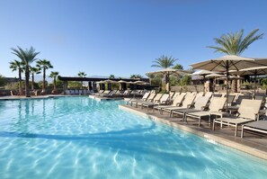 Une piscine entourée de palmiers, avec des chaises longues et des parasols.