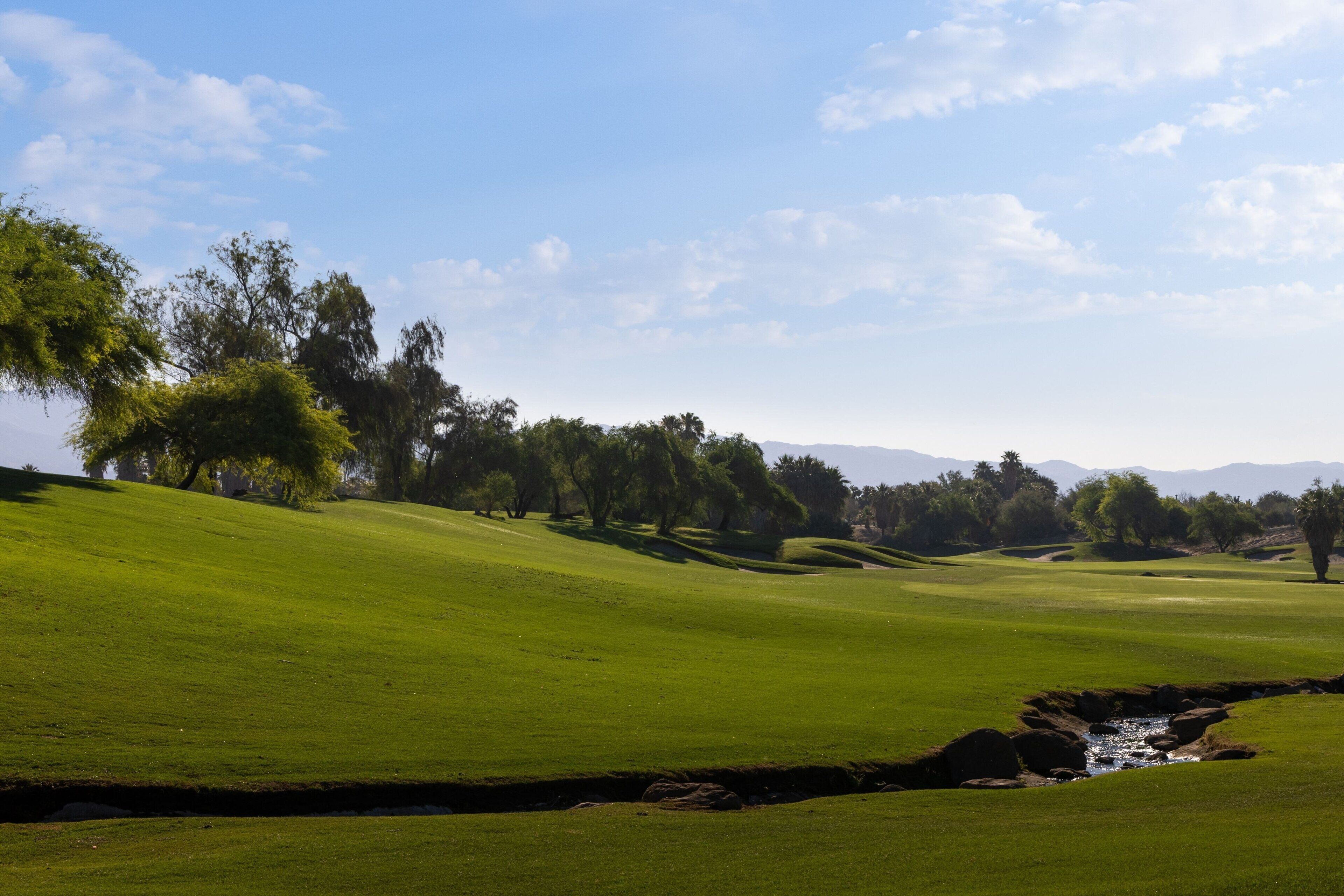 A golf course with rolling green hills, a stream, and trees.