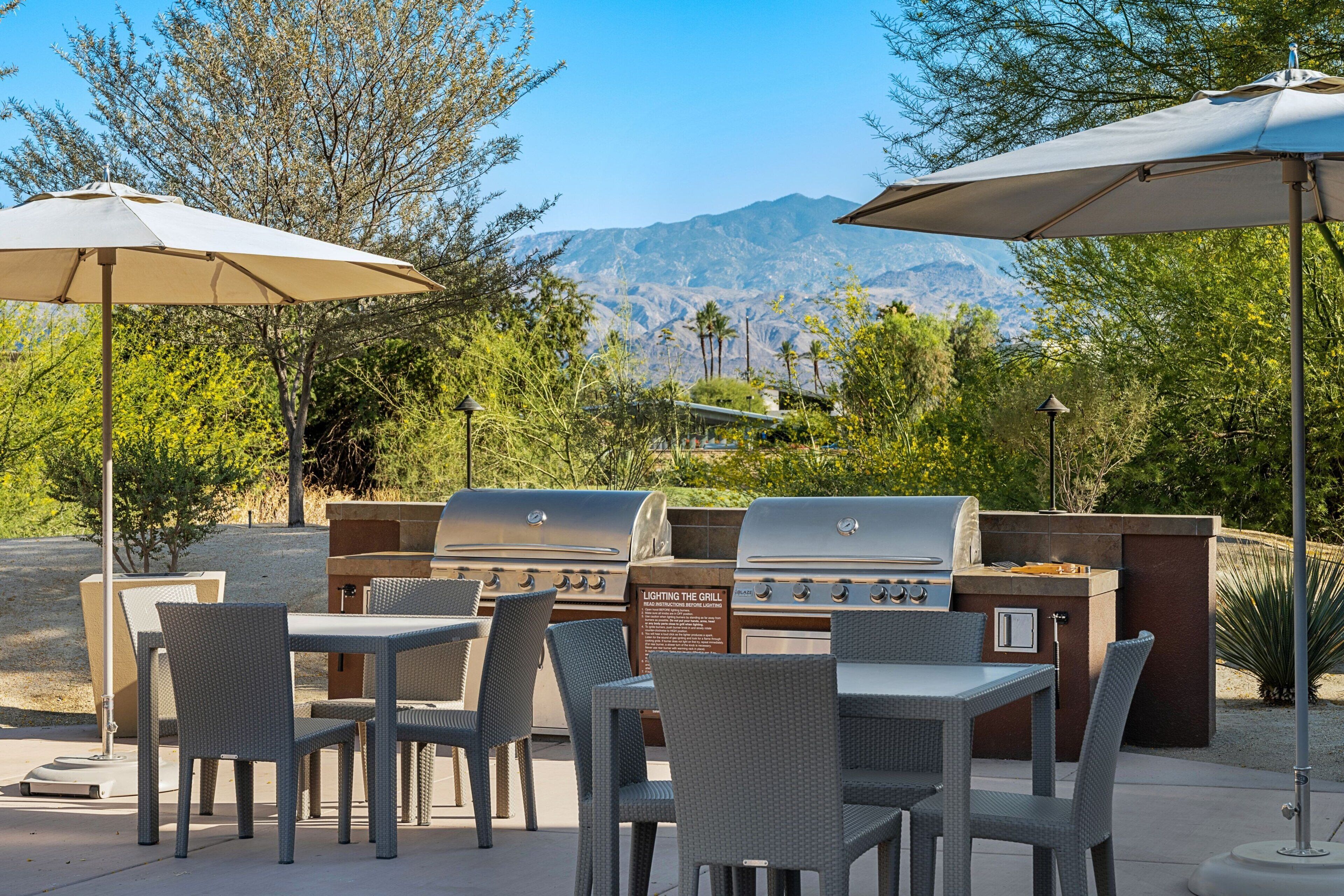 An outdoor patio with a grill, wicker chairs, and umbrellas.