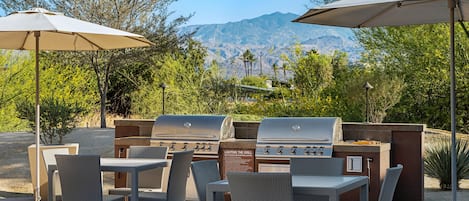 An outdoor patio with a grill, wicker chairs, and umbrellas.
