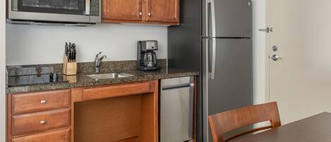 A compact kitchen with wooden cabinets, a stainless steel refrigerator, a built-in microwave, a coffee maker, and a dishwasher.