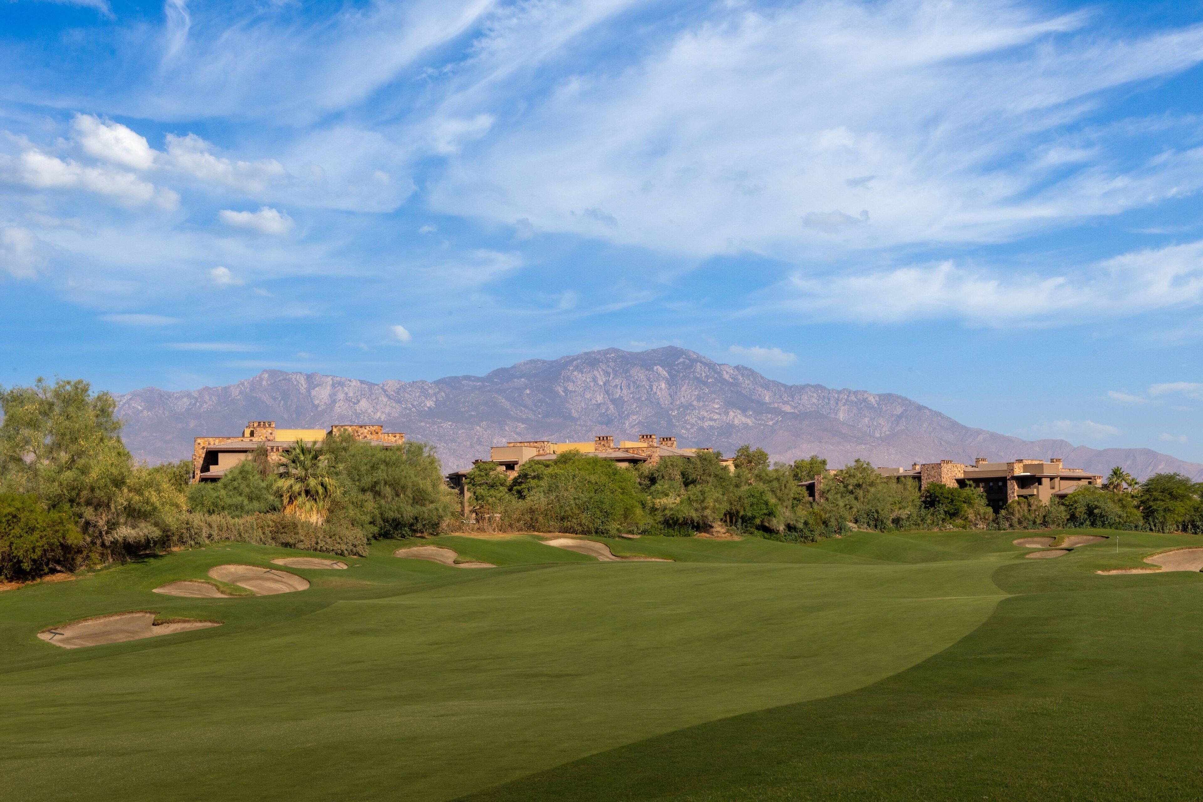 A golf course with bunkers, a clear sky, and mountains in the background.
