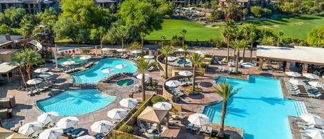 A resort with multiple swimming pools, sun loungers, and a golf course in the background.