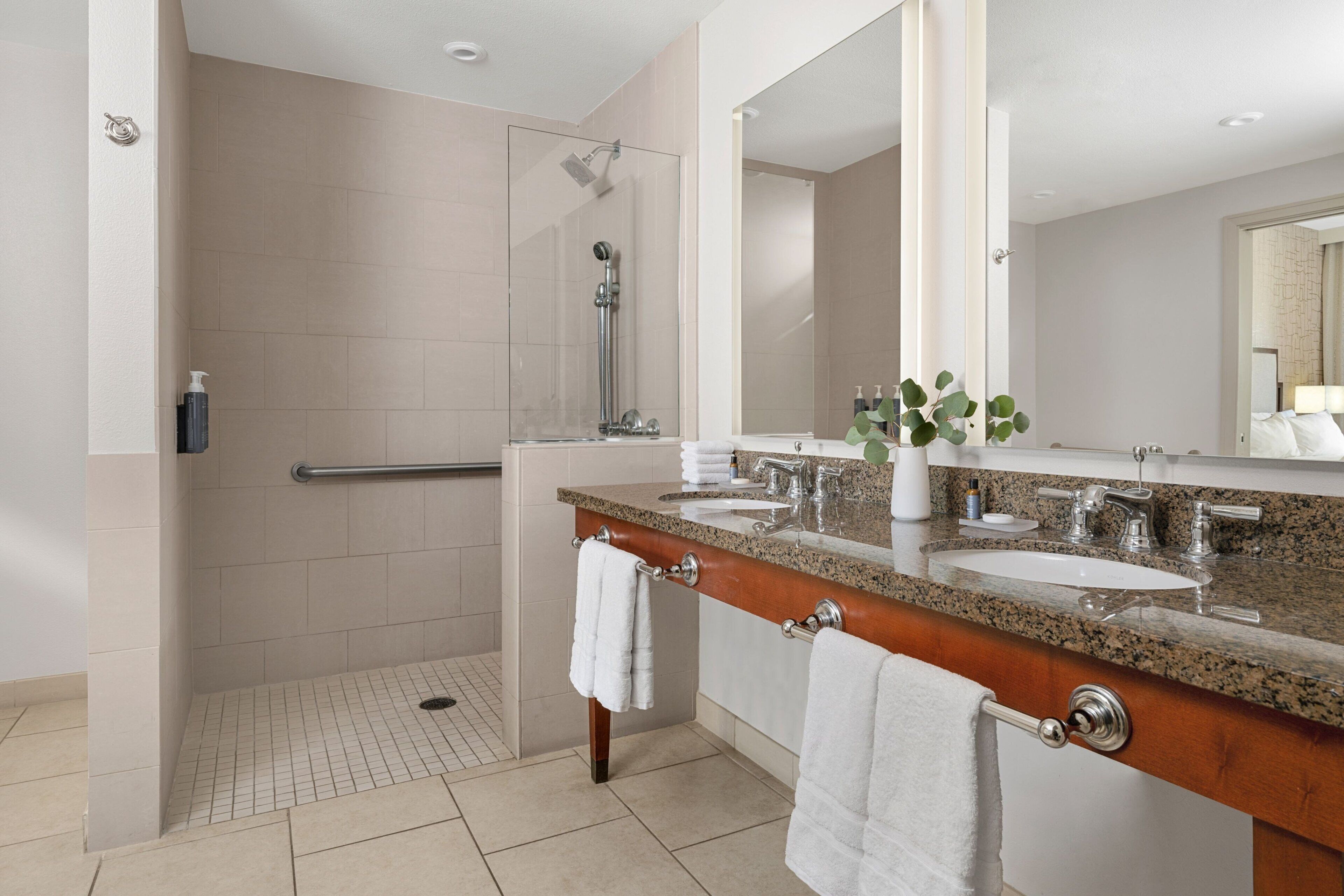 A modern bathroom with two sinks, a shower, and a large mirror.