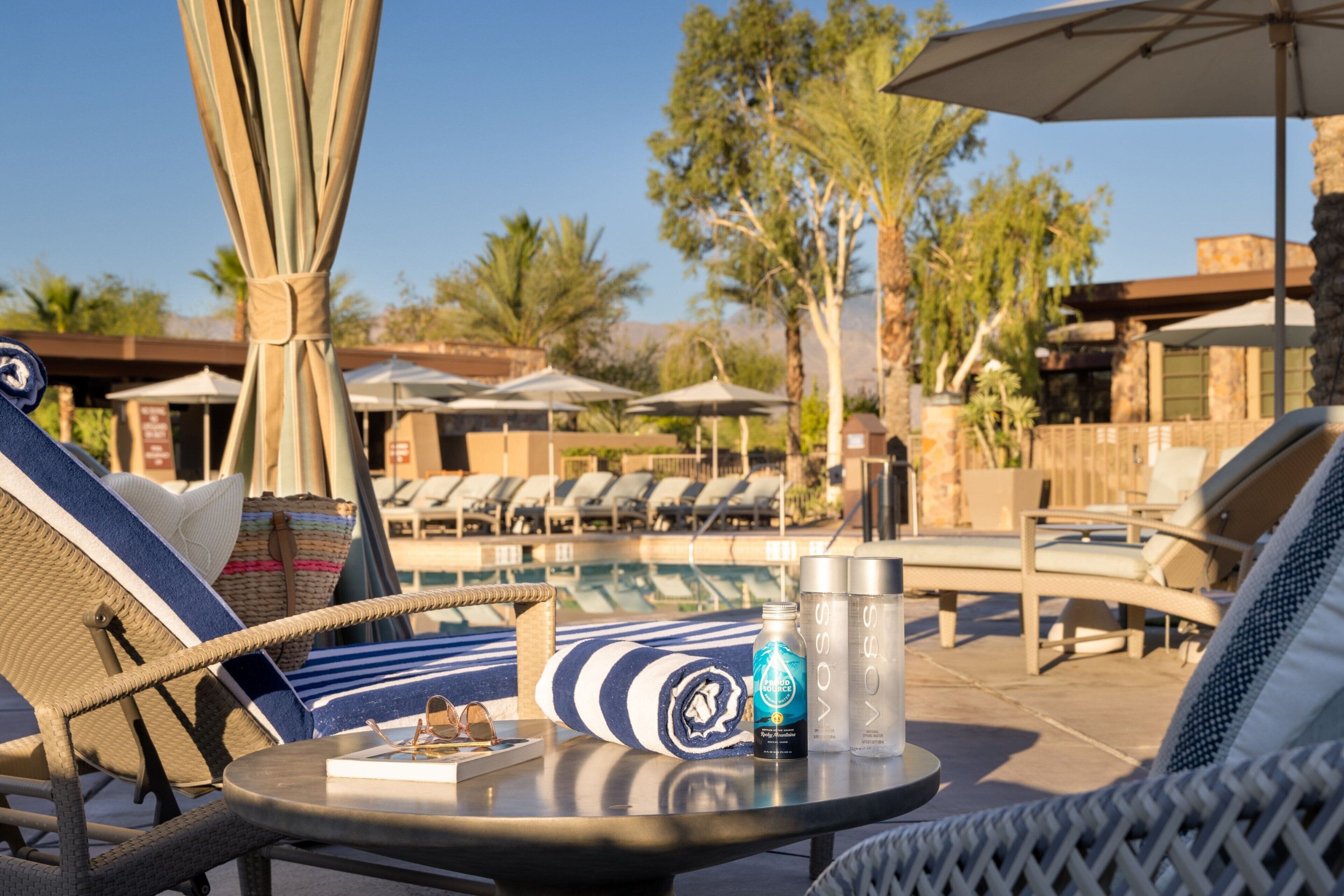 A poolside area with lounge chairs, umbrellas, and a table with a bottle and glasses.