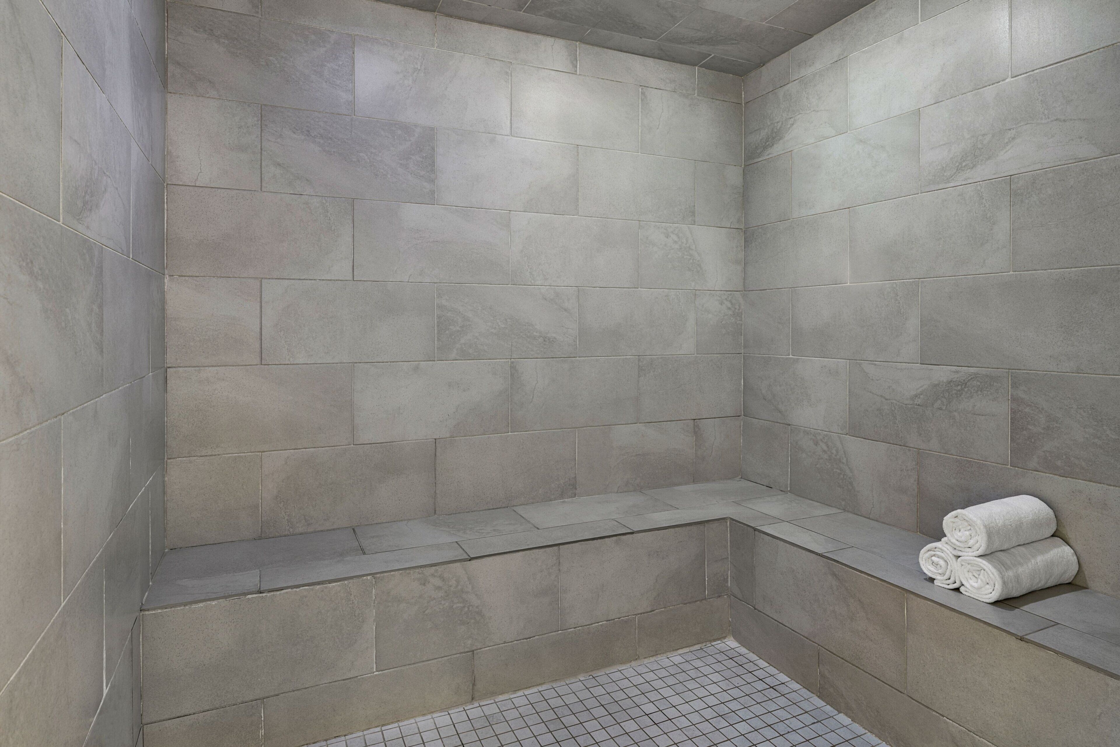 A corner shower with grey tiles and a built-in bench.