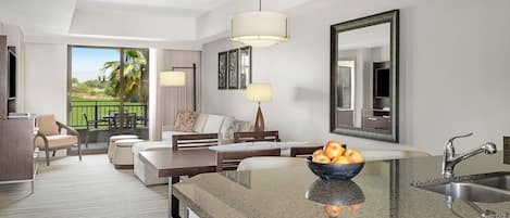 A modern hotel room with a kitchen area, a dining area with a sofa and chairs, a large mirror, and a view of the outdoors.