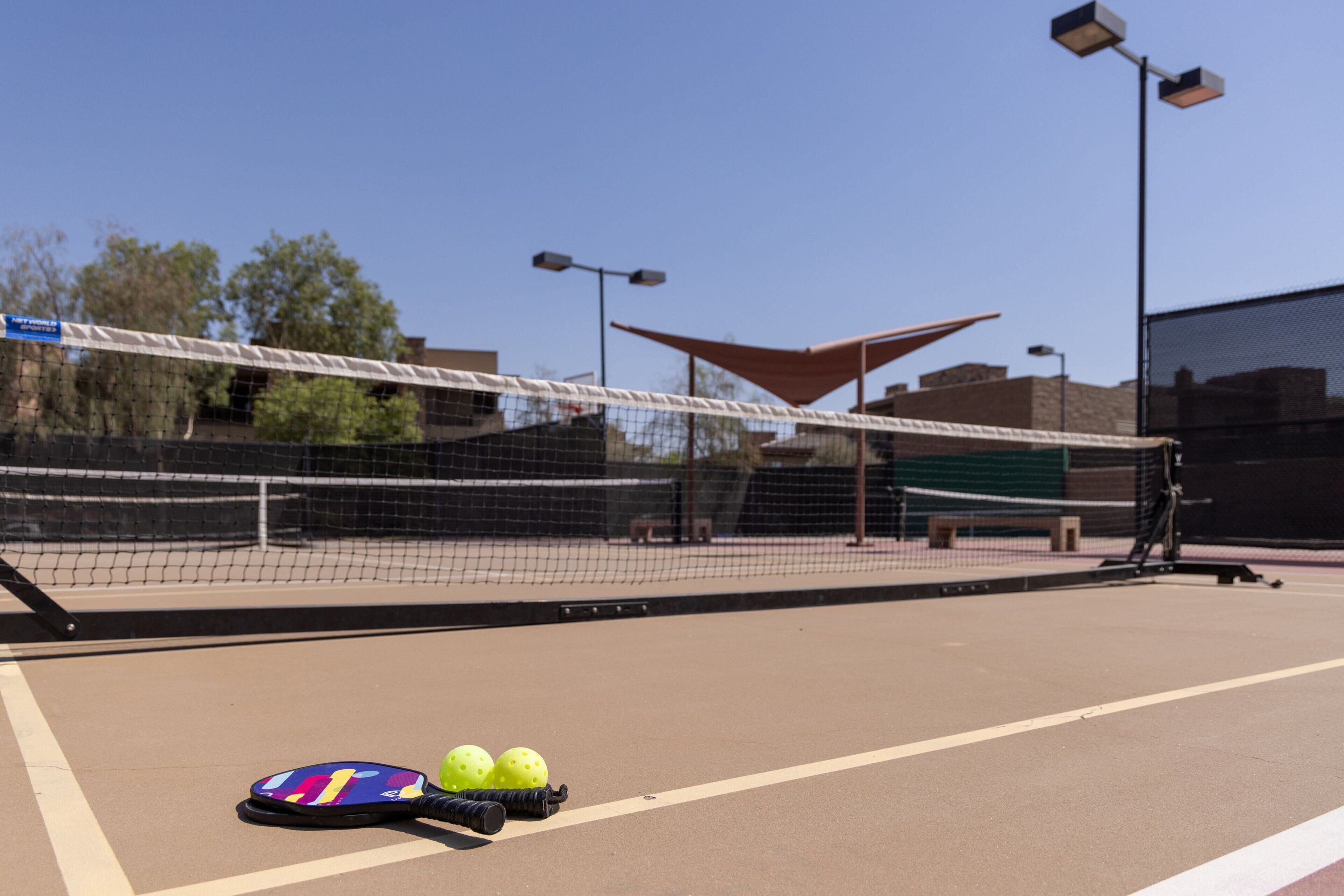 A tennis court with a net, a tennis racket, and two tennis balls.