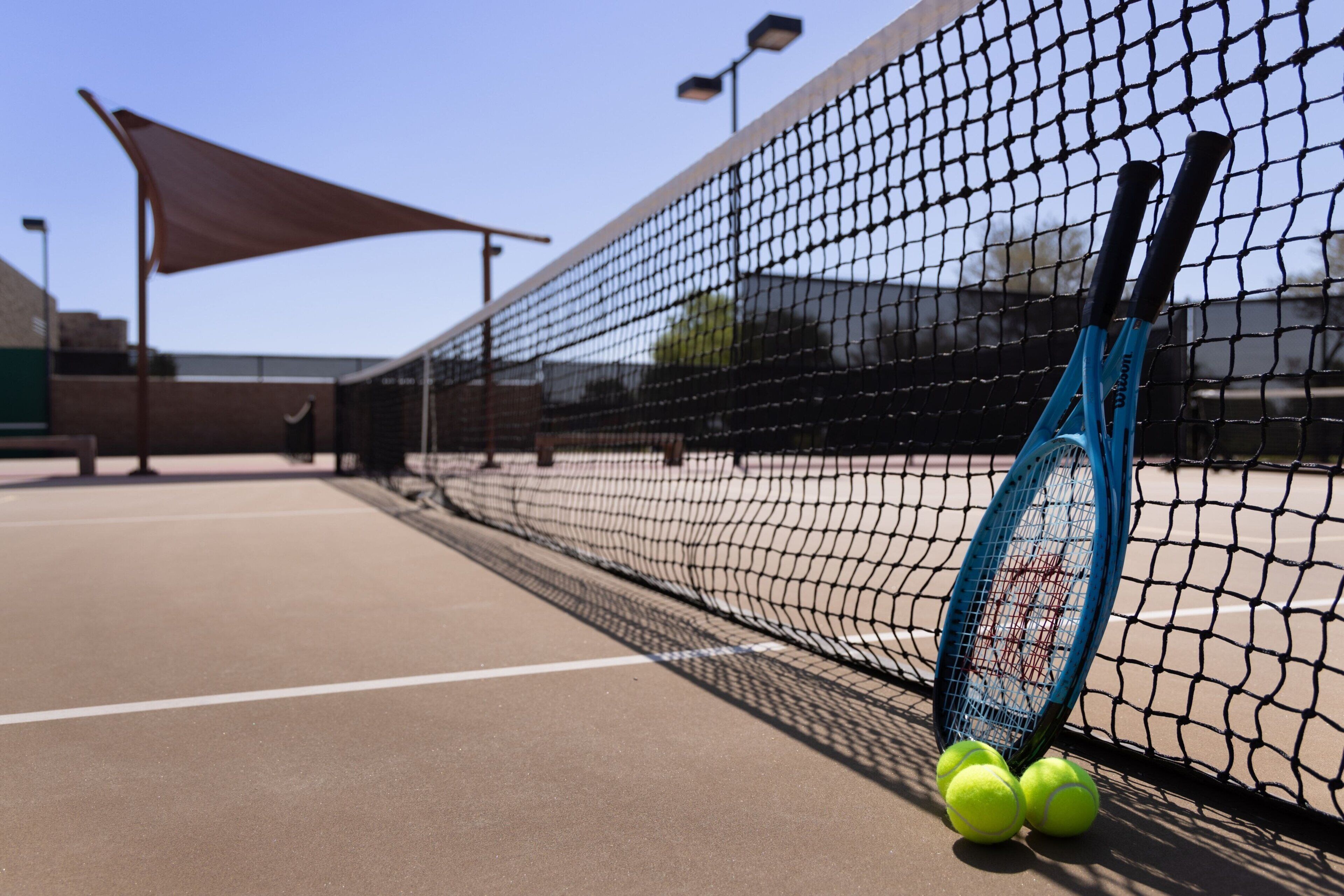 A tennis court with a net, a tennis racket, and three tennis balls.