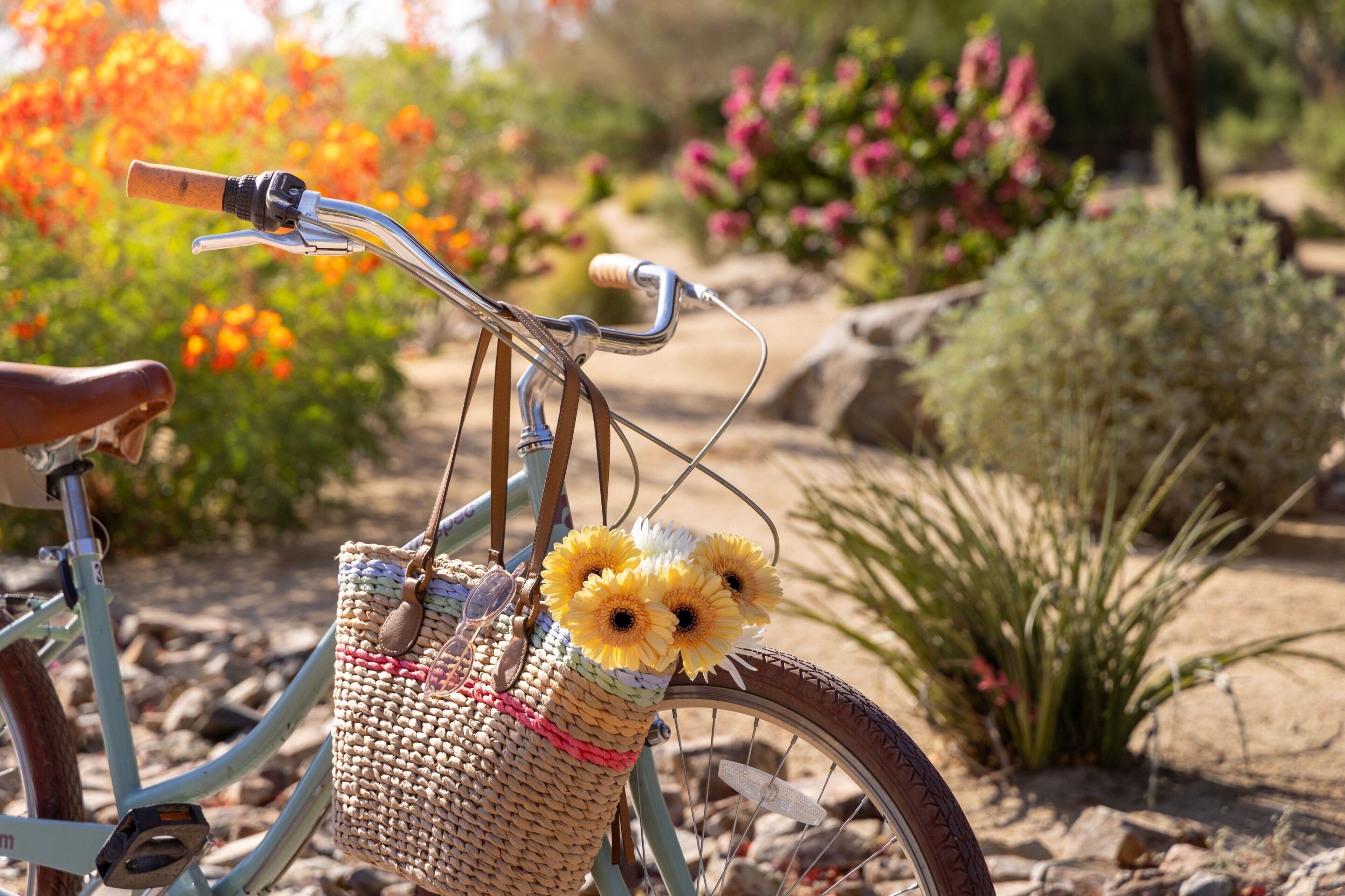 A bicycle with a basket containing sunflowers and a woven bag, set against a garden backdrop.