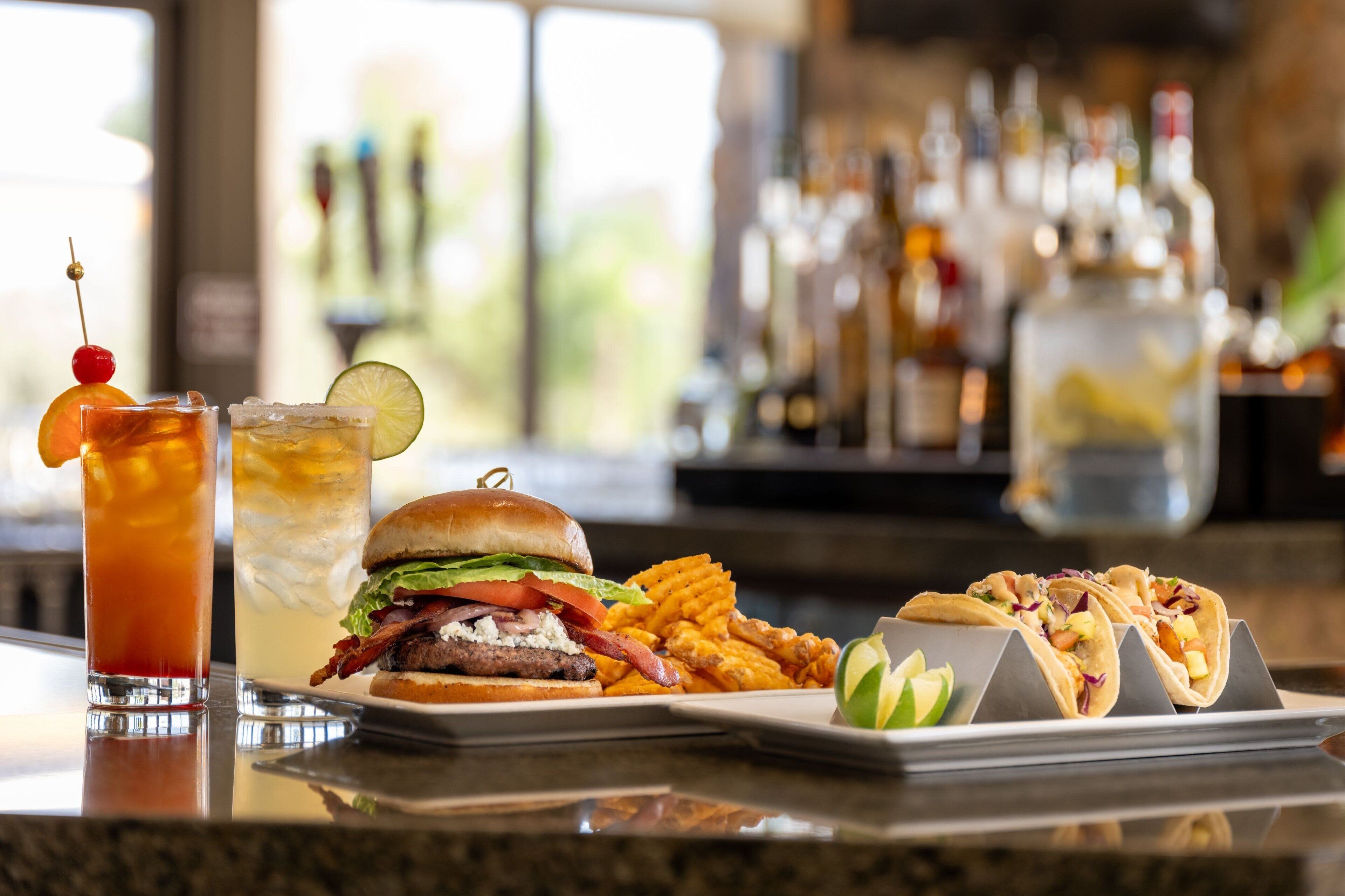 A bar area with a variety of drinks, a burger, fries, and tacos.