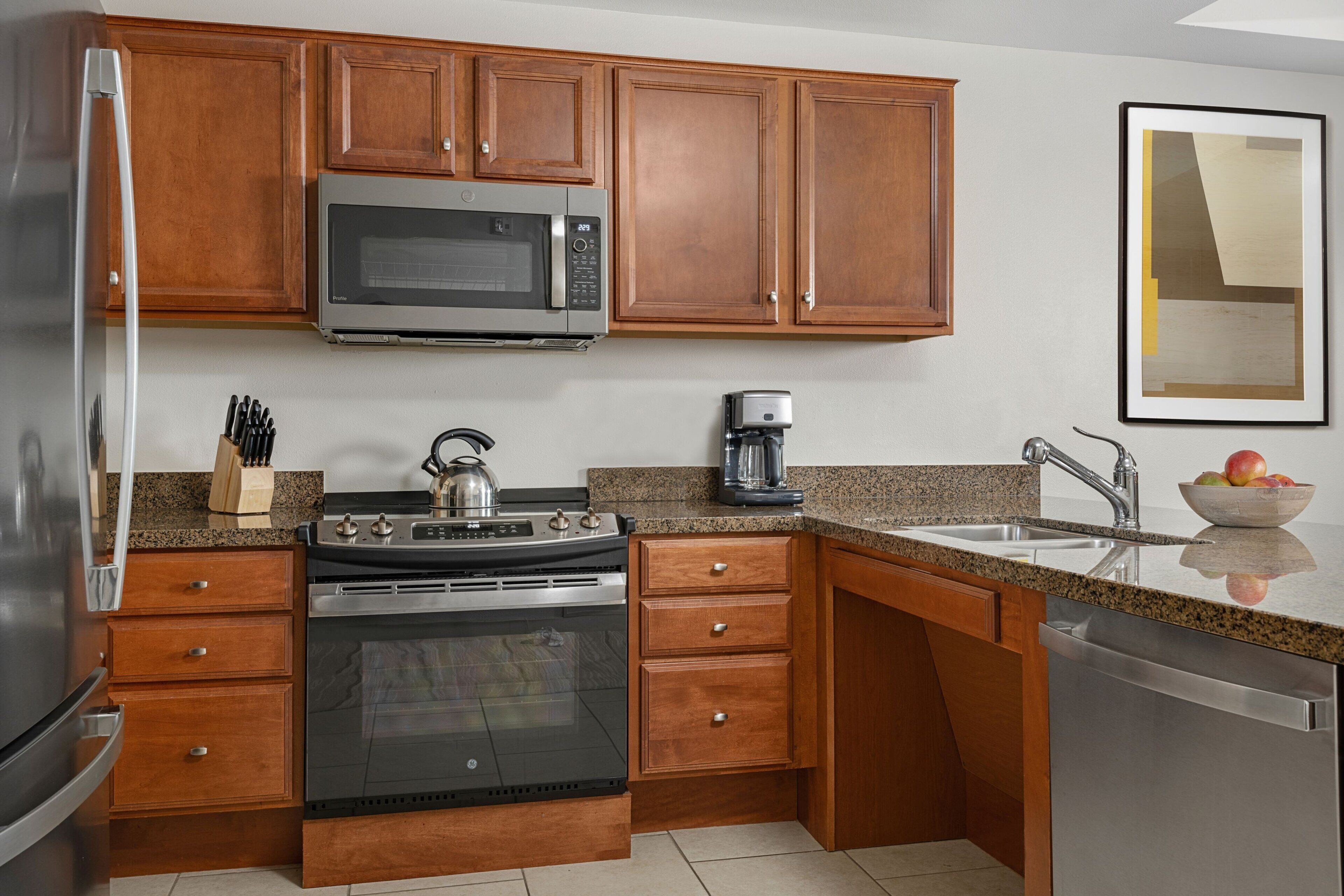 Una cocina con armarios de madera, un refrigerador de acero inoxidable, un microondas, una estufa y un lavavajillas.