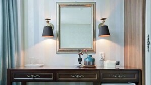 A hotel room with a wooden desk, two wall-mounted lamps, a mirror, a small table with a vase, and a green ottoman. - Central Tourist Hotel (Seoul)