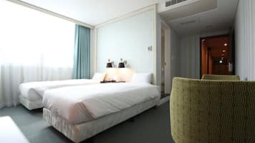 A hotel room with two single beds, a chair, a nightstand, and a window with curtains.