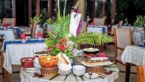 A dining table set with various dishes, a centerpiece with flowers, and a buffet area in a restaurant. - Castello Beach Hotel (Praslin Island)
