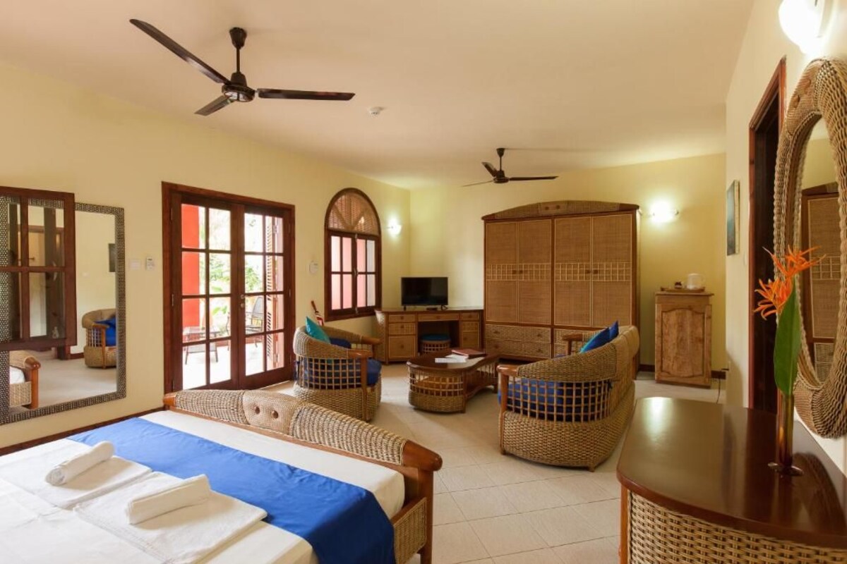 A hotel room with a bed, two wicker chairs, a TV, a wardrobe, and a ceiling fan.