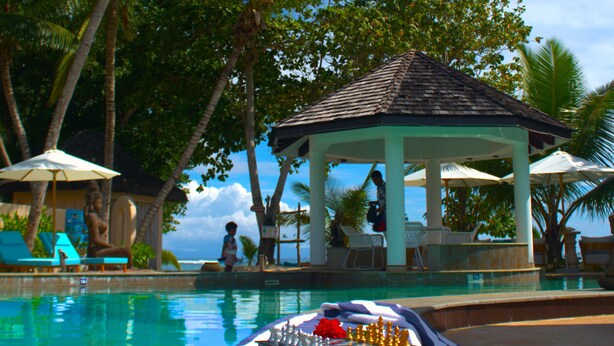 A pool area with palm trees, a gazebo, and a chessboard. - Castello Beach Hotel (Praslin Island)