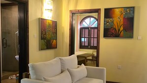 A white sofa in a room with a shower, a door with shutters, and two paintings on the wall. - Castello Beach Hotel (Praslin Island)