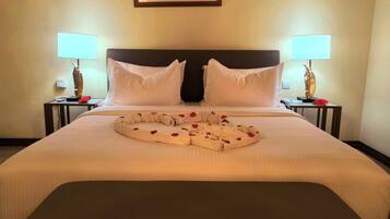 Een hotelkamer met een groot bed, twee nachtkastjes met lampen, een lijst aan de muur en een decoratieve kussenset op het bed.