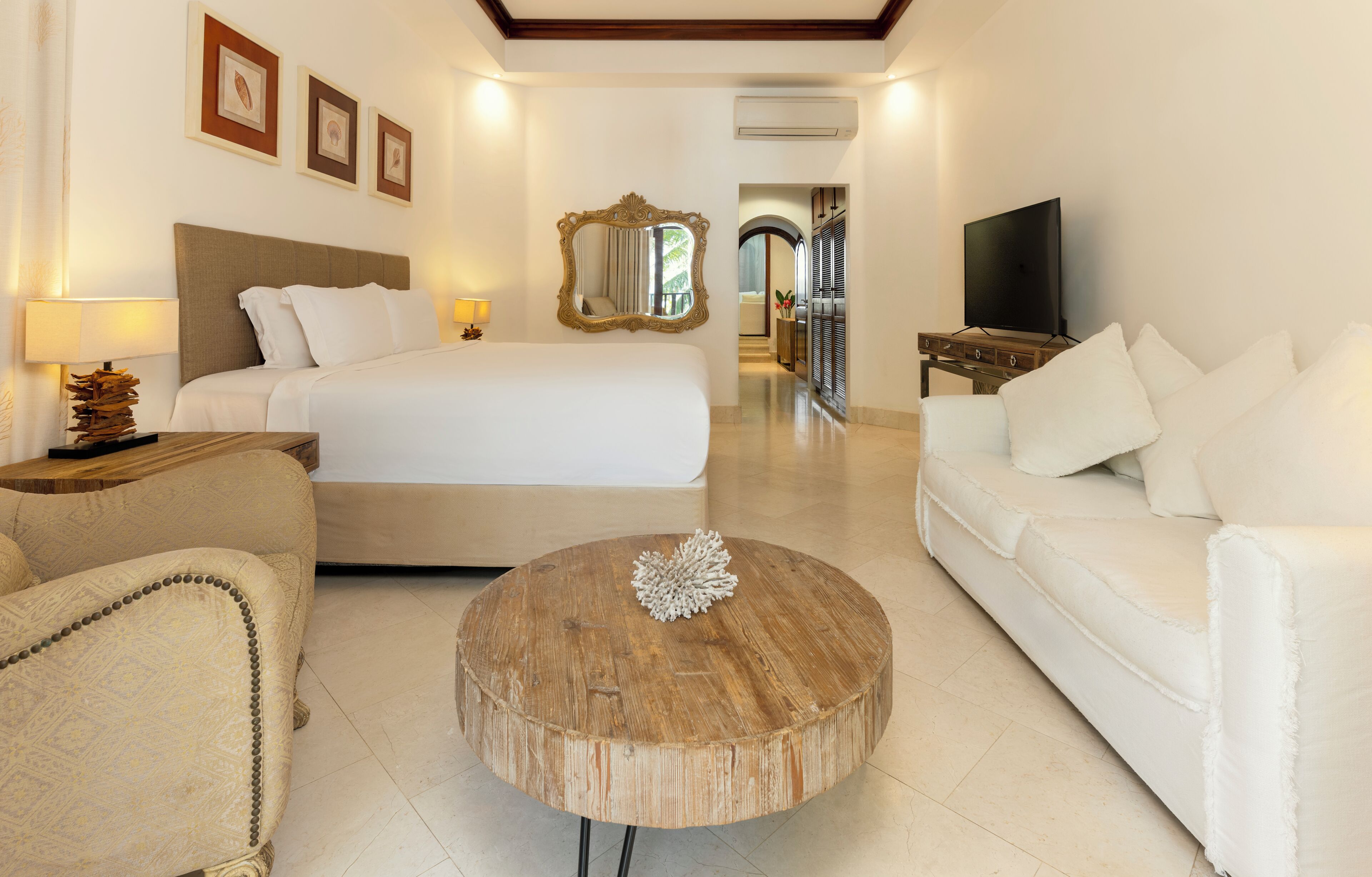 A hotel room with a bed, a sofa, a round wooden coffee table, a TV, and a mirror.